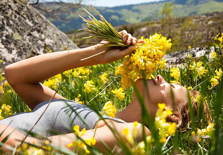Eine Frau auf einer Wiese riecht an Blumen